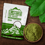 Green BC Kratom Bag laying on a wooden table next to a bowl of Green Maeng Da Kratom Powder