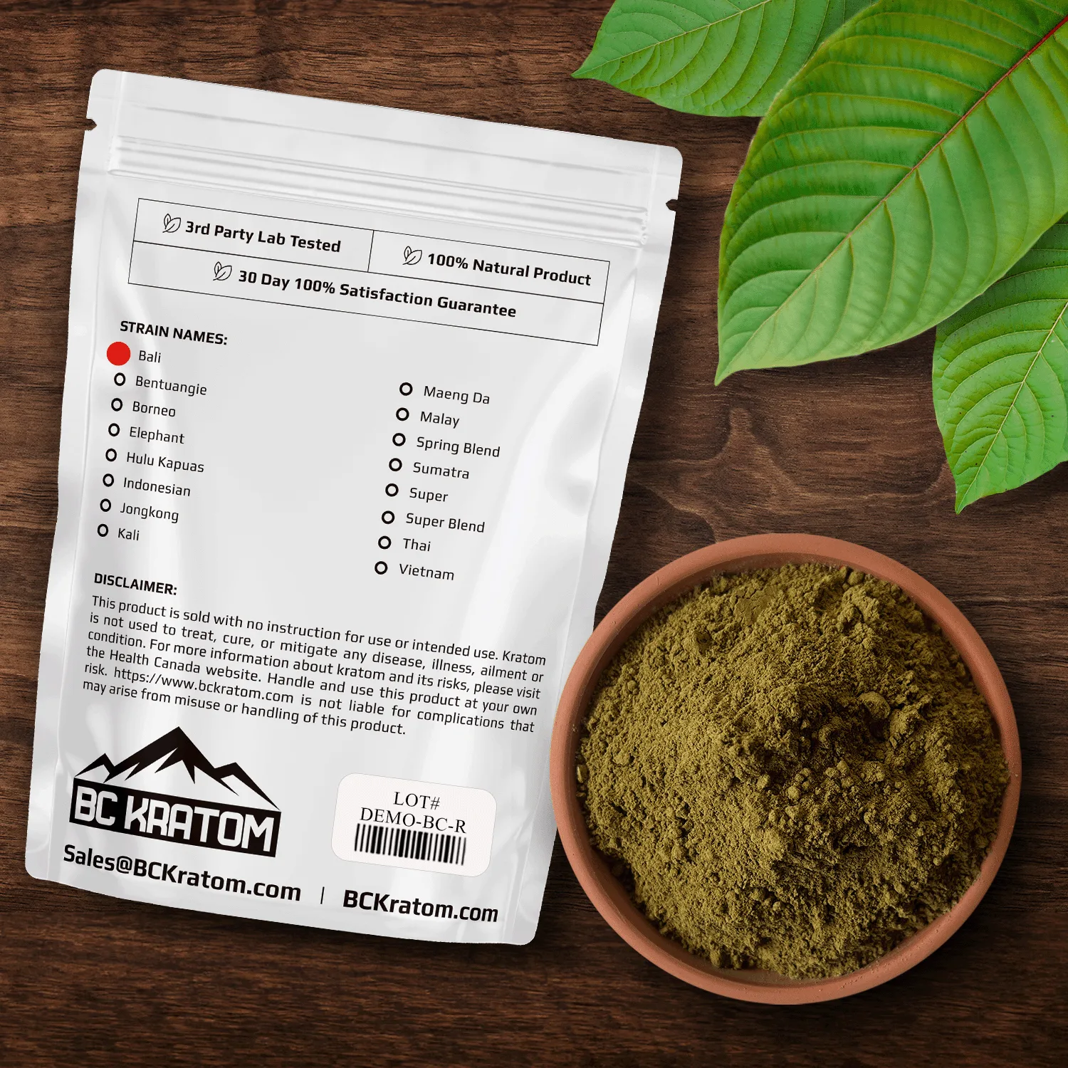 BC Kratom Red Bali Kratom Bag with a bowl of kratom powder laying on a wooden table with red vein leaves