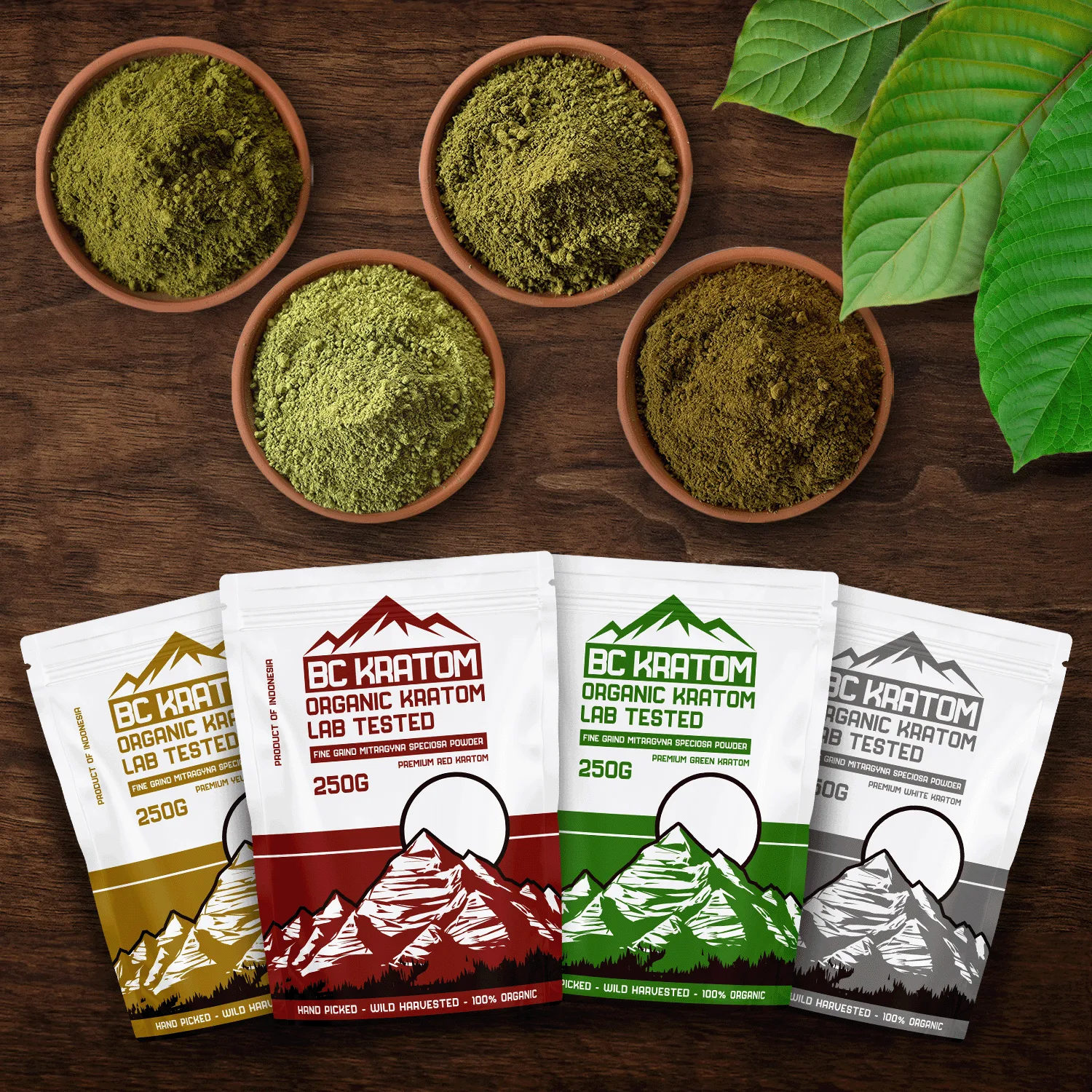 4x 250g BC Kratom bags laying on a wooden table beside four different bowls of kratom powder.