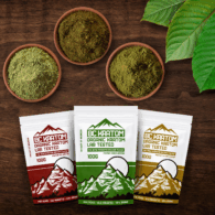 three 100g BC Kratom bags laying on a wooden table beside 3 different bowls of kratom powder