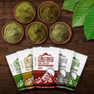 5 x 100g BC Kratom bags laying on a wooden table next to five different bowls of kratom powder