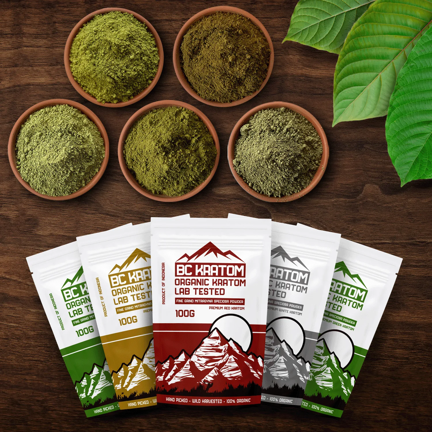 5 x 100g BC Kratom bags laying on a wooden table next to five different bowls of kratom powder