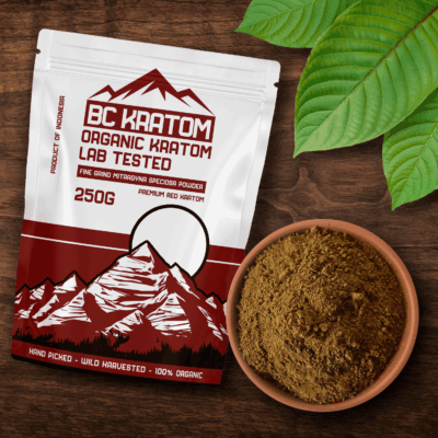 Red BC Kratom bag laying on a wooden table next to a bowl of Super Red Kratom powder