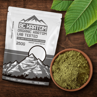 White BC Kratom bag laying on a wooden table next to a bowl of White Indonesian Kratom powder