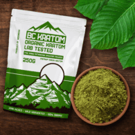 Green BC Kratom Bag laying on a wooden table next to a bowl of Super Blend Kratom Powder