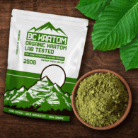 Green BC Kratom Bag laying on a wooden table next to a bowl of Green Jongkong Kratom Powder