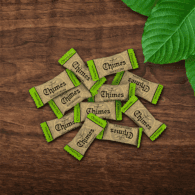 Pile of individually wrapped Original Ginger Chimes candies loosely laid down on a wooden table with leaves.