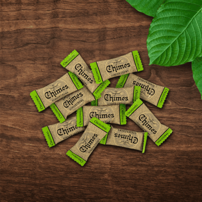 Pile of individually wrapped Original Ginger Chimes candies loosely laid down on a wooden table with leaves.